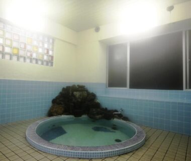 Round indoor tiled bath with rock feature at Sunrise Meiji-ya in Nagano