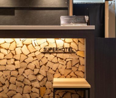 Reception counter with stacked firewood wall and Super Hotel Asahikawa sign in Hokkaidō