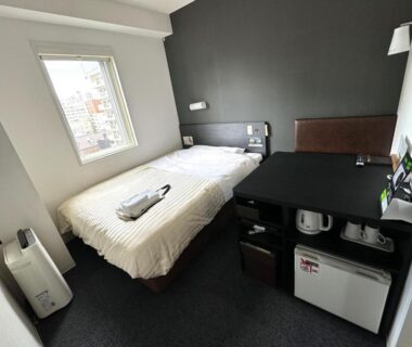 Small guest room with single bed, desk, mini fridge and window at Super Hotel Asahikawa, Hokkaidō