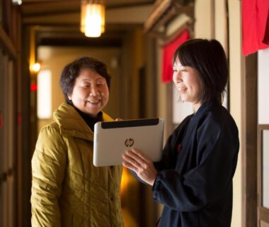 Ryokan staff showing guest a tablet in corridor at Super Hydrogen Rich Spa Yado Kanzan, Gunma