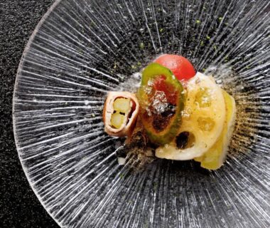 Delicate small plated dish on radiating glass plate with vegetable garnishes and sauce, refined ryokan presentation
