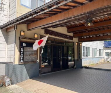 Wooden canopy entrance with Japanese flag and glass doors at Suzuki Ryokan in Hokkaidō
