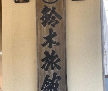 Vertical wooden signboard with kanji at Suzuki Ryokan entrance flanked by wall lanterns