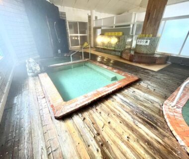 Wooden-floor indoor onsen baths with tiled pools and large windows at Suzuki Ryokan, Hokkaidō