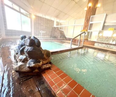 Indoor tiled onsen baths at Suzuki Ryokan in Hokkaidō with wooden deck and rock feature