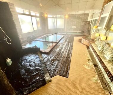 Indoor onsen room with tiled floor, wooden decking, washing stations and windows at Suzuki Ryokan, Hokkaidō