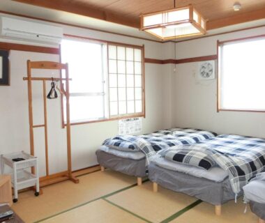 Tatami room with three single beds, shoji screens and wooden clothes rack at Suzukisou Kyoto