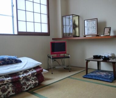 Tatami room with futon, shoji screens, low table, floor cushion and small television at Suzukisou Kyoto