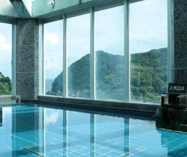Tiled indoor onsen bath with large windows overlooking verdant mountain slopes at Suzunami ryokan in Mie, Kansai