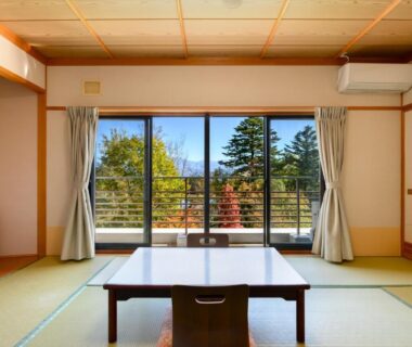Traditional tatami room with low table and zaisu chair, sliding doors opening to balcony and treed view