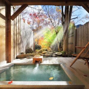 Sunlit outdoor wooden onsen tub with stone garden and maple leaves at Syoubun, Gunma, Kantō