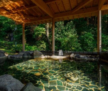 Covered stone onsen with wooden roof and surrounding greenery at TAKITEI Riverside Onsen, Kanazawa Ishikawa
