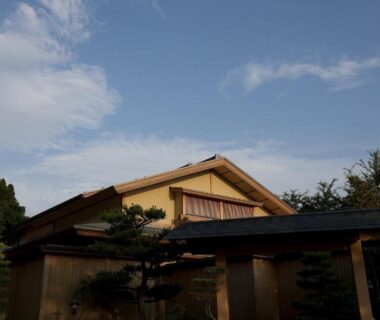 Wooden ryokan exterior with entrance gate and trees at TAKITEI Riverside Onsen in Ishikawa