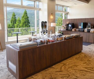 Bright dining area with buffet island, coffee station and large windows overlooking forested hills at TAOYA Gero in Gifu
