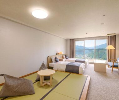 Spacious guest room with elevated tatami seating, twin beds and large window overlooking green hills in Gifu