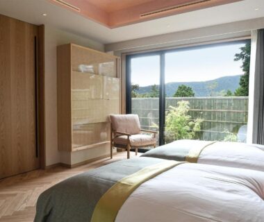 Bright twin bedroom with parquet floor, armchair and balcony overlooking wooded hills in Hakone, Kanagawa