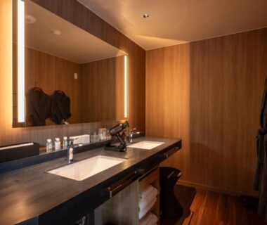 Illuminated wooden vanity and sink with mirror, toiletries and hanging robes at THE YUKAWA Ichijoh Branch, Miyagi