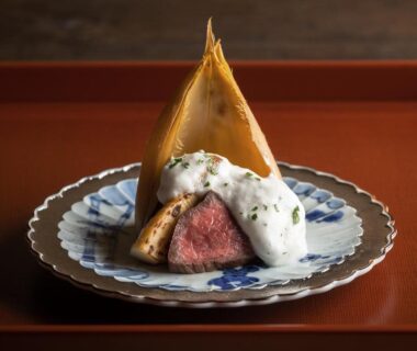 Seared beef with airy white foam and bamboo sheath on a blue ceramic plate on lacquer tray