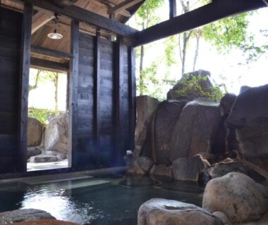 Rock-lined indoor onsen with wooden walls at Tabinoyado Asonoyu, Kumamoto, Kyūshū