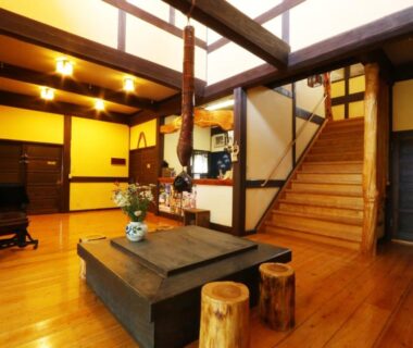Spacious wooden lobby with low hearth table, exposed beams and staircase at Tabinoyado Asonoyu in Kumamoto