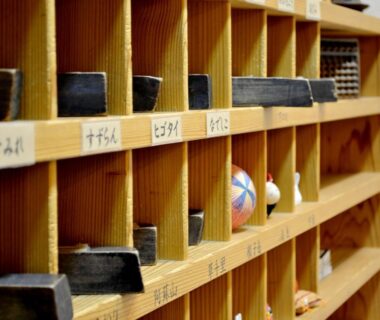 Wooden cubbies with labeled slots and small personal items at Tabinoyado Asonoyu in Kumamoto