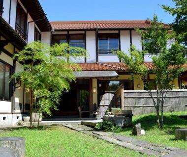 Traditional two-story ryokan exterior with stone path and garden at Tabinoyado Asonoyu, Kumamoto, Kyūshū, Japan
