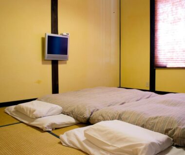 Tatami room with futons, pillows, wall-mounted TV and window at Tabinoyado Asonoyu, Kumamoto