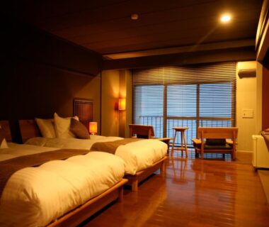 Low wooden-floor twin room with shoji screens and seating at Tabinoyado Ushionoakari Geiboso, Mie