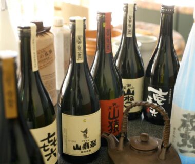 Selection of sake bottles and a teapot on a wooden table at Tabinoyado Ushionoakari Geiboso, Mie