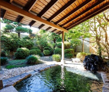 Covered outdoor onsen bath at Tabist Chikuba Shinyotei Hakodate Yunokawaonsen, Hokkaidō, with garden, rocks, and wooden roof