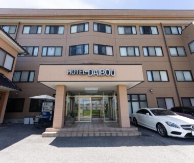 Beige hotel entrance with glass doors, HOTEL DAIBOU sign and parked car at Tabist Daibou Ichihara in Chiba