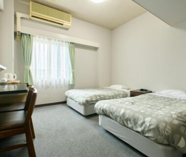 Twin room with two single beds, desk, air conditioner and green curtains at Tabist Hotel Seishokan, Shizuoka