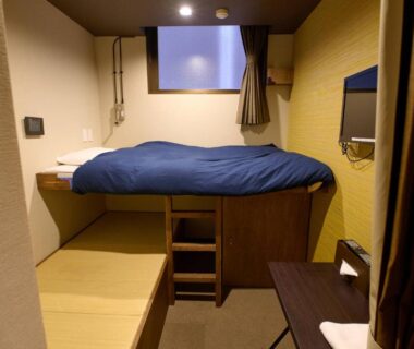 Compact room with raised bed, tatami platform, ladder and wall TV at Tabist Hotel Seishokan in Shizuoka