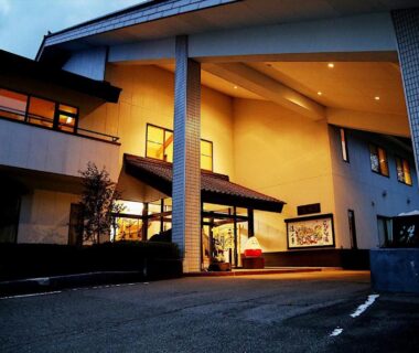 Illuminated ryokan entrance with covered driveway and warm lighting at Tabist Koboshi no Yu Senshintei in Fukushima