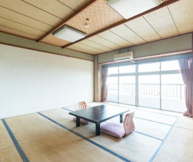 Traditional tatami room with low table and floor cushions, sliding balcony doors at Tabist Miyoshi Ryokan, Kanagawa