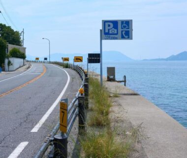 Coastal road with seawall and parking sign beside calm sea near Tabist Setouchinoyado Takehara Seaside, Hiroshima, Chūgoku