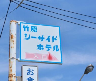 Weathered roadside sign for Takehara Seaside hotel against blue sky with utility wires in Hiroshima