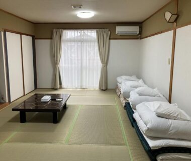 Spacious tatami room with stacked futons, low table and sliding doors at Tabist Yamaga Onsen Yuyado Izumi, Kumamoto Kyūshū Japan