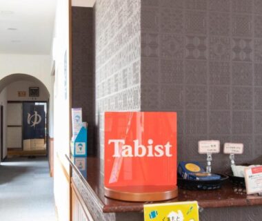 Reception counter with Tabist bag and brochures, corridor leading to onsen entrance marked by yu sign