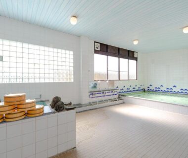 Tiled communal indoor onsen with wooden buckets and large windows at Tabist Yamaga Onsen Yuyado Izumi Kumamoto