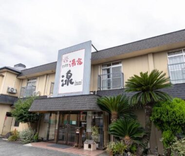 Two-story ryokan facade with entrance, signboard, shrubs and parking in Yamaga, Kumamoto