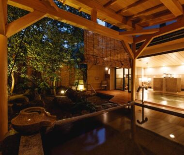 Covered wooden veranda with onsen bath beside a garden, warm lantern lighting and traditional ryokan interior