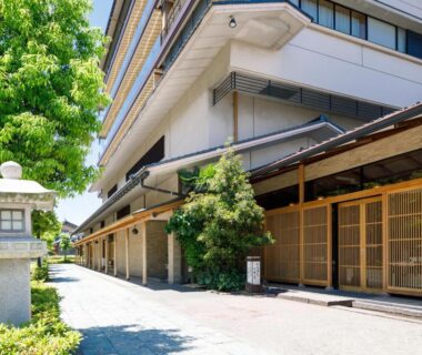 Exterior entrance with wooden lattice doors, stone lantern and shaded walkway at Tachibana Shikitei in Ishikawa, Chūbu, Japan