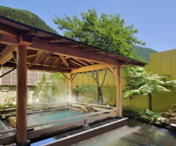 Wooden covered outdoor onsen bath with garden and steam at Tachibanaya, Yamagata
