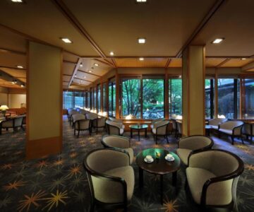 Spacious lounge with cushioned chairs, low tables and large windows overlooking a garden at Tachibanaya in Yamagata