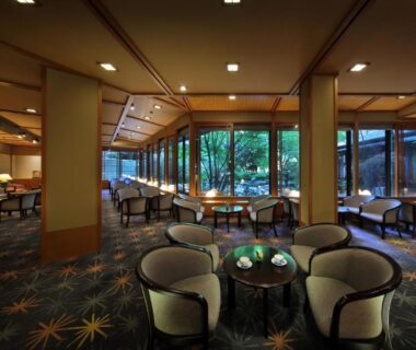 Spacious lounge with cushioned chairs, low tables and large windows overlooking a garden at Tachibanaya in Yamagata