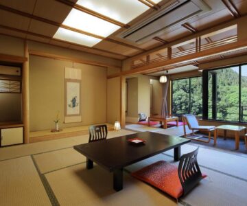 Traditional tatami room with low table, zabuton cushions and large window overlooking green hillside at Tachibanaya, Yamagata