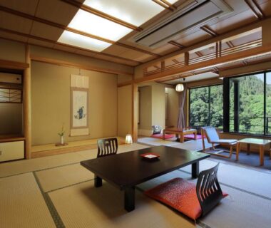 Traditional tatami room with low table, zabuton cushions and large window overlooking green hillside at Tachibanaya, Yamagata