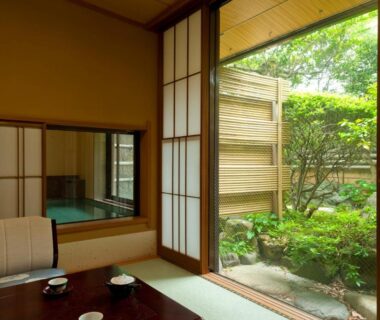 Tatami room with low table, shoji screens, indoor wooden bath visible and sliding door to small garden