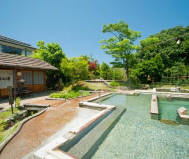 Series of outdoor onsen pools with wooden walkways beside ryokan building and garden at Tagawa Ryusenkaku, Ishikawa, Chūbu